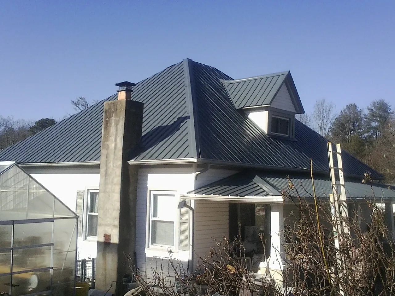 Dark blue standing seam metal roof on a white farmhouse with dormer — Slate & Tile Roof Repair by Roofing Brothers in Welch