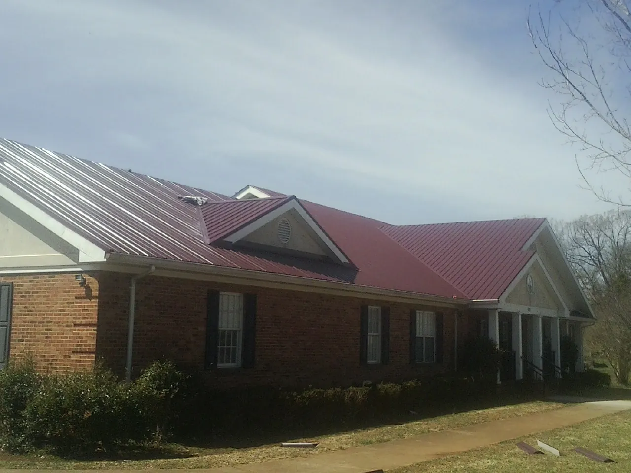 Red metal roof with gabled entries on a long brick building, from a Hail Damage Roof Repair job in Welch