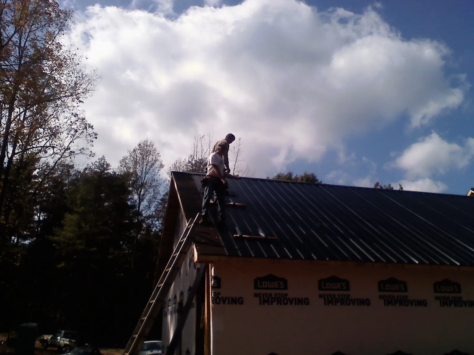 Roofer fastening dark metal panels high against a cloudy sky, from a Roof Inspection job in Welch